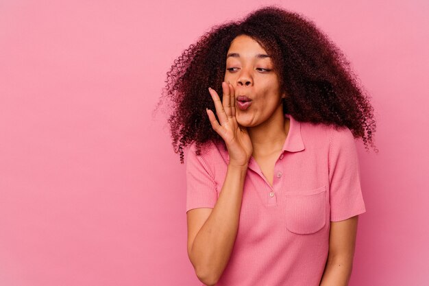 La giovane donna afroamericana isolata sul rosa sta dicendo una notizia segreta di frenata calda e sta guardando da parte