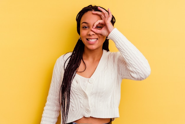 La giovane donna afroamericana isolata sulla parete gialla ha eccitato mantenendo il gesto giusto sull'occhio.