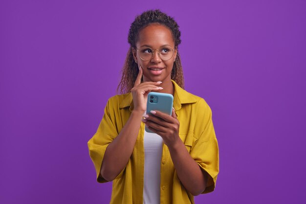 La giovane donna afroamericana positiva con il telefono tocca pensieroso il mento