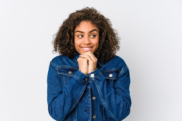 La giovane donna afroamericana tiene le mani sotto il mento, sta guardando felicemente da parte.