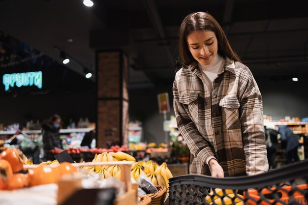 La giovane donna al supermercato compra le banane