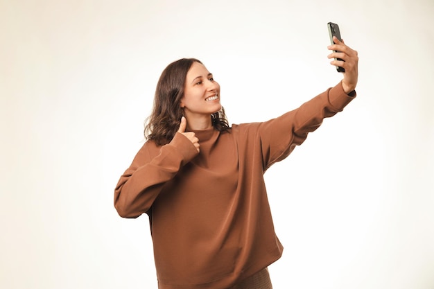 La giovane donna allegra che tiene il pollice in su sta prendendo un selfie con un telefono