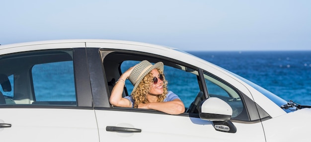 La giovane donna allegra e felice sorride e si diverte a viaggiare con l'auto Oceano blu e cielo sullo sfondo Persone di sesso femminile sedute e ammirate fuori dal finestrino del veicolo Persone e trasporti Vacanze estive