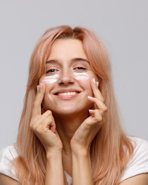 la giovane donna allegra positiva applica la crema da giorno nutriente di sollevamento idratante o il trattamento facciale