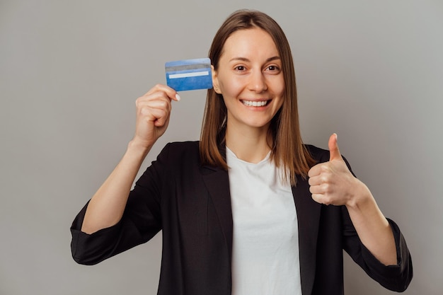 La giovane donna allegra sta alzando il pollice e raccomanda una carta di credito blu