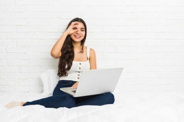 La giovane donna araba che lavora con il suo computer portatile sul letto ha eccitato mantenendo il gesto giusto sull'occhio.