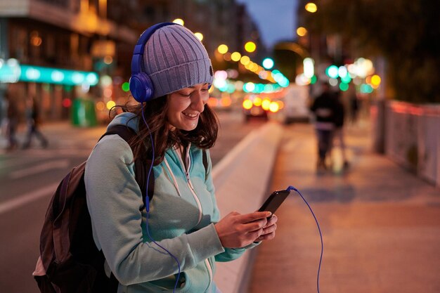 La giovane donna ascolta la musica sulle cuffie con le luci della città al crepuscolo