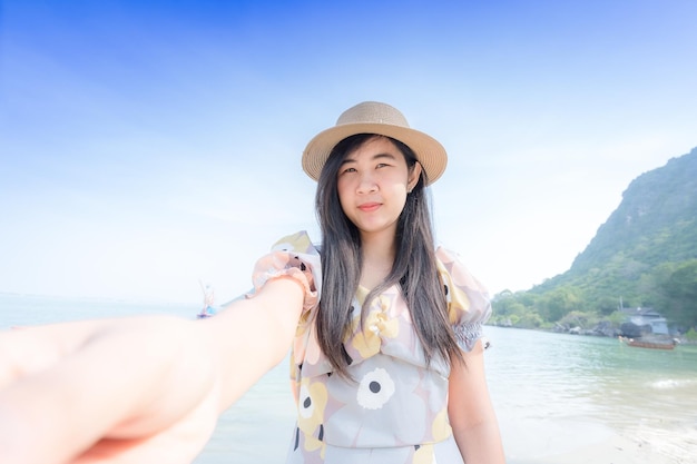 La giovane donna asiatica attraente che indossa il sorriso bianco del vestito gode con le vacanze estive sulla sensazione della spiaggia