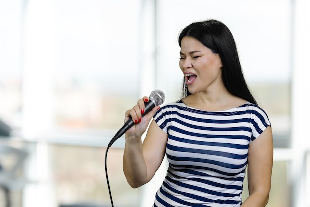 La giovane donna asiatica castana sta cantando una canzone con il microfono sfocato sfondo luminoso