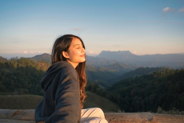 La giovane donna asiatica che irradia felicità è seduta in cima alla montagna e al caldo sole la sera al parco nazionale