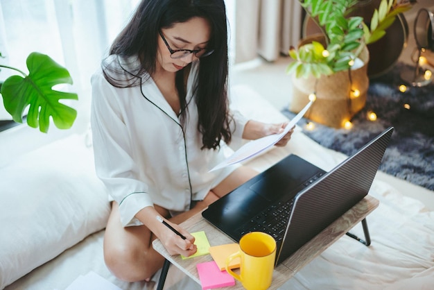 La giovane donna asiatica che lavora come freelance lavora sul computer portatile a casa lavorando dal concetto di casa