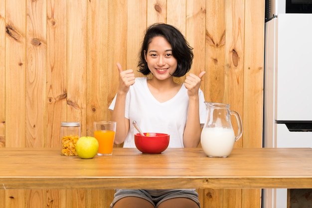 La giovane donna asiatica che mangia il latte della prima colazione pollici aumenta il gesto