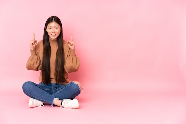 La giovane donna asiatica che si siede sul pavimento ha isolato che indica su una grande idea