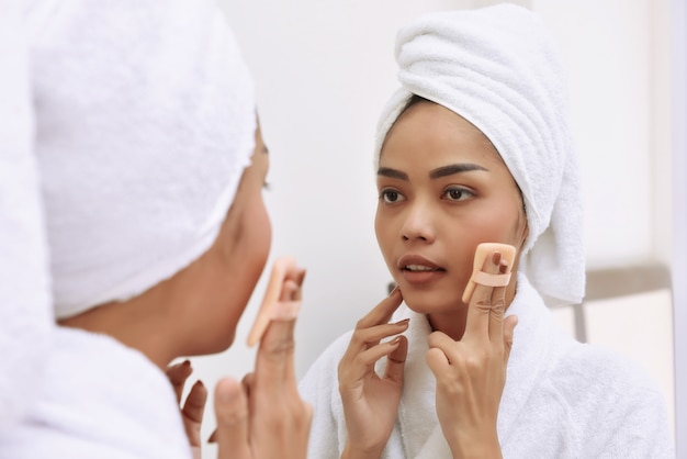 La giovane donna asiatica con gli asciugamani di bagno pulisce il suo fronte