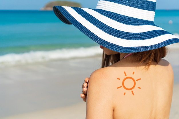 La giovane donna asiatica con la forma del sole sulla spalla applica la crema solare sulla spalla Concetto di estate sulla spiaggia