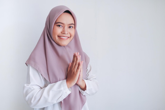 La giovane donna asiatica dell'Islam che indossa il velo dà il saluto alle mani con un grande sorriso sul viso Donna indonesiana su sfondo grigio Eid Mubarak saluto