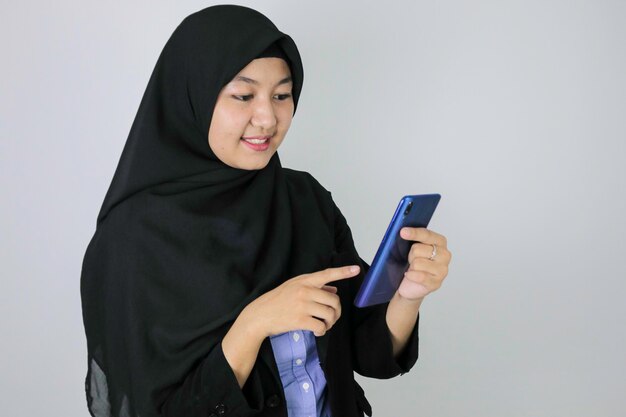 La giovane donna asiatica dell'Islam che indossa il velo è sorridente e felice in ciò che vede sullo smartphone Donna indonesiana su sfondo grigio