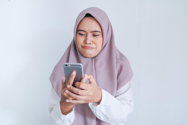 La giovane donna asiatica dell'Islam che indossa il velo è triste e piange per ciò che vede sullo smartphone Donna indonesiana su sfondo grigio