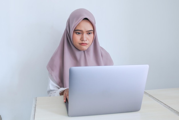 La giovane donna asiatica dell'Islam che indossa il velo è un aspetto serio al laptop Donna indonesiana su sfondo grigio