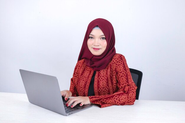 La giovane donna asiatica dell'Islam è seduta, si diverte e sorride quando si lavora su un computer portatile su sfondo bianco