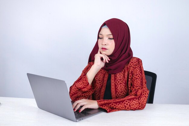 La giovane donna asiatica dell'Islam ha un aspetto serio con un gesto di pensiero mano sul viso sulla parte anteriore del laptop