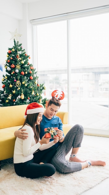 La giovane donna asiatica felice che indossa il cappello di Babbo Natale sorprende il suo ragazzo con un regalo di Natale.