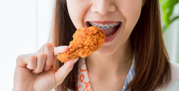 La giovane donna asiatica felice che tiene il pollo fritto per mangia.