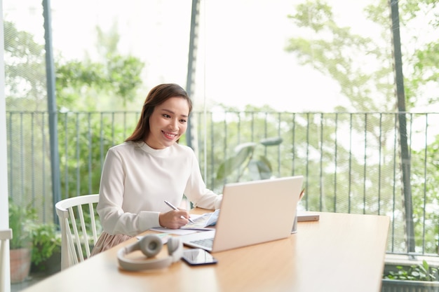 La giovane donna asiatica felice si rilassa che si siede sullo scrittorio fa il lavoro in Internet