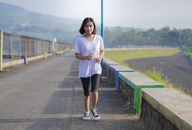 La giovane donna asiatica fitness sta correndo e facendo jogging per un allenamento all'aperto sulla strada al mattino