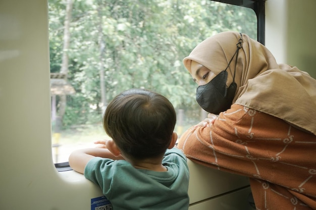 La giovane donna asiatica in hijab e suo figlio parlano e guardano fuori dal finestrino all'interno del treno