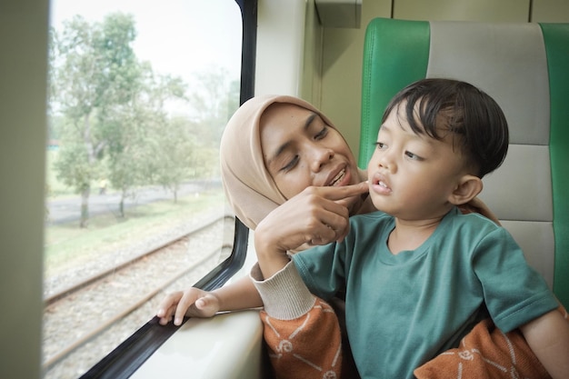 La giovane donna asiatica in hijab e suo figlio parlano e guardano fuori dal finestrino all'interno del treno