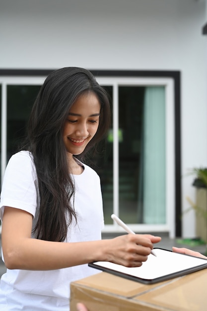 La giovane donna asiatica riceve la scatola dal fattorino e firma sulla tavoletta digitale.