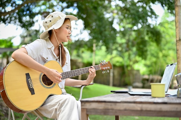 La giovane donna asiatica rilassata e felice canta una canzone mentre suona la chitarra nel giardino del campeggio