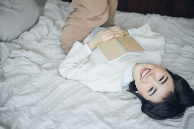 La giovane donna asiatica sta leggendo un libro in camera da letto.