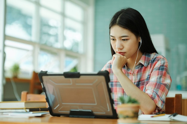 La giovane donna asiatica studia davanti al computer portatile e usa le cuffie su offsitexA