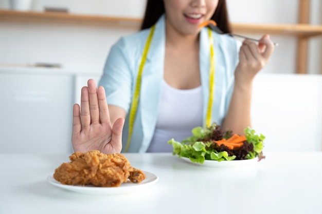 La giovane donna asiatica sulla dieta e sulla scelta mangia l'insalata di verdure dal pollo fritto dei rifiuti industriali, stante a dieta e concetto di buona salute