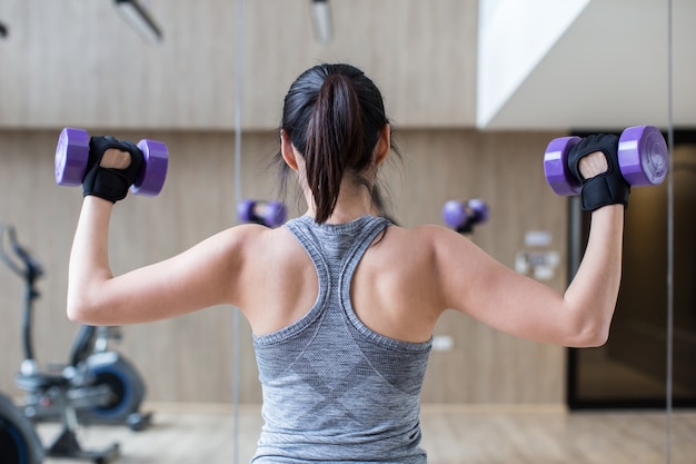 La giovane donna asiatica tiene l'allenamento con i manubri in palestra