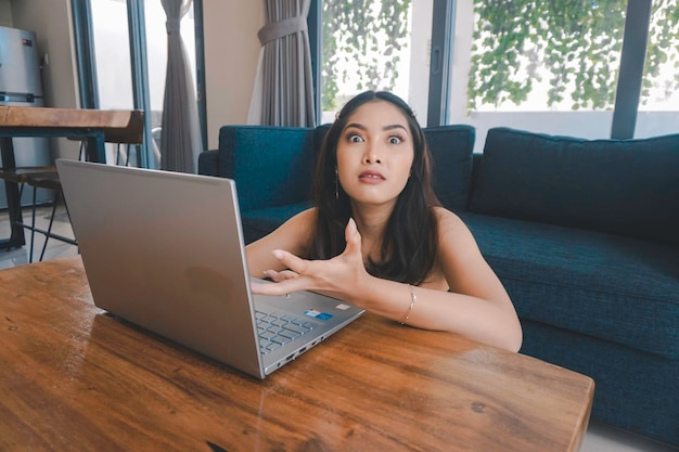 La giovane donna asiatica trascorre il suo tempo a casa seduta in soggiorno frustrata e stanca a lavorare sul suo laptop