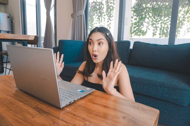 La giovane donna asiatica trascorre il suo tempo a casa seduta su un comodo divano nel soggiorno con una conferenza online sul suo laptop