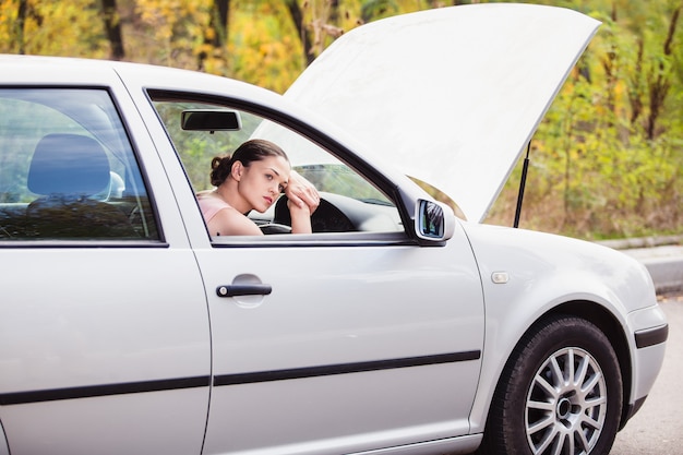 La giovane donna attende assistenza vicino alla sua auto, che si è rotta sul lato della strada