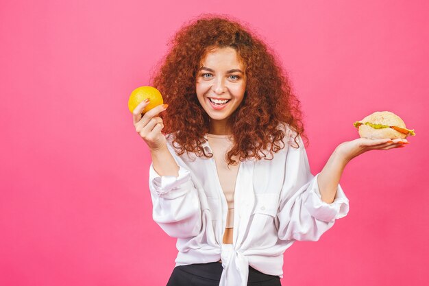 La giovane donna attraente fa una scelta tra cibo sano e malsano