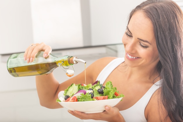 la giovane donna attraente versa l'olio d'oliva in una sana insalata di verdure