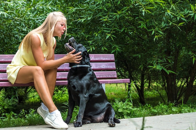 La giovane donna bacia il suo grosso cane nero su una panchina nel parco