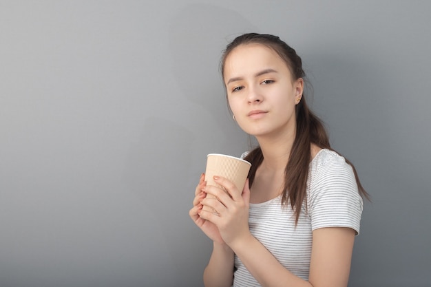 La giovane donna beve il caffè su fondo grigio