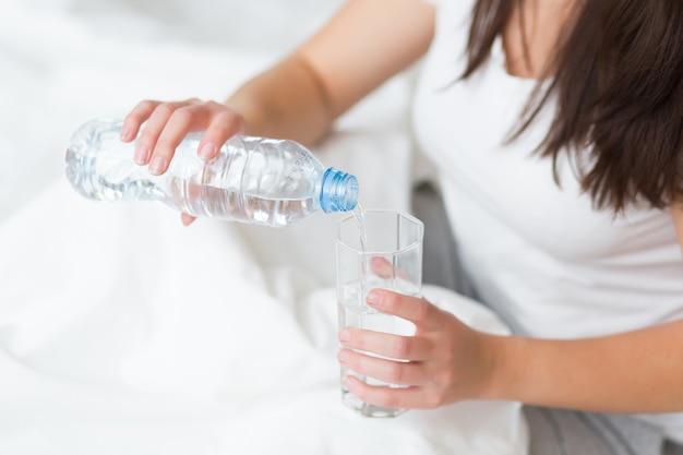 La giovane donna beve un bicchiere d'acqua al mattino, concetto di stile di vita sano