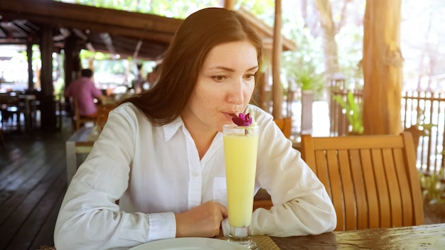 La giovane donna beve un cocktail di frutta in un caffè.