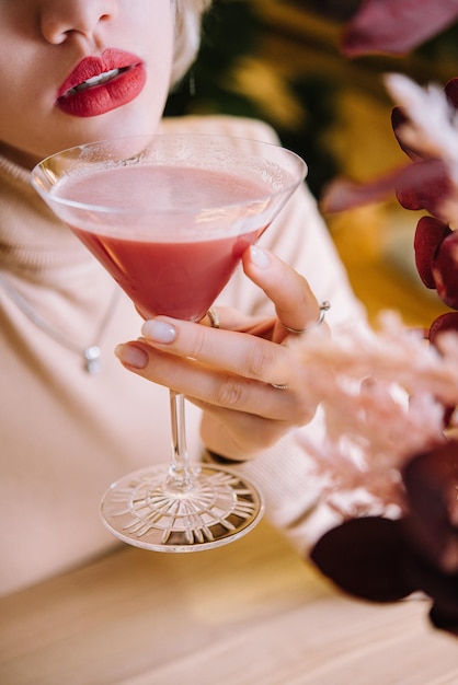 La giovane donna beve un cocktail rosso con la fragola