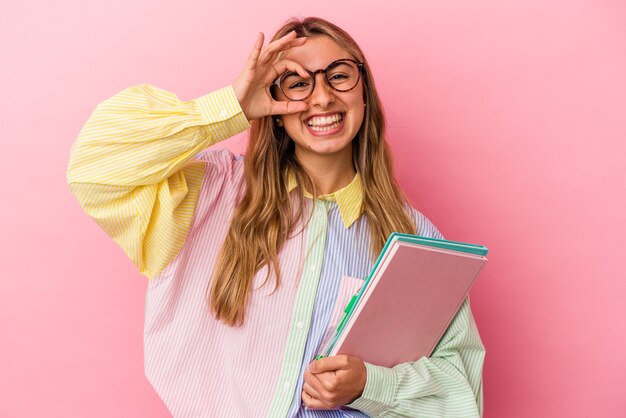 La giovane donna bionda caucasica dello studente che tiene i libri ha isolato eccitato mantenendo il gesto giusto sull'occhio