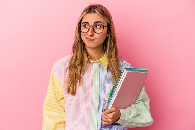 La giovane donna bionda caucasica dello studente che tiene i libri isolati confusa, si sente dubbiosa e insicura.