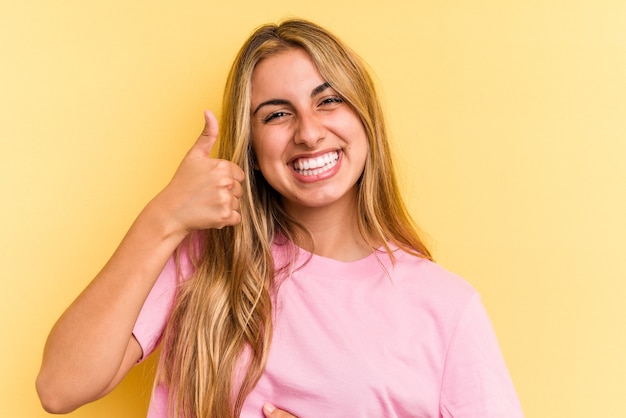 La giovane donna bionda caucasica isolata su fondo giallo tocca la pancia, sorride dolcemente, mangia e concetto di soddisfazione.